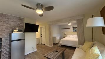 Une chambre d’hôtel compacte comprenant un coin cuisine, un lit, une table de chevet, un ventilateur de plafond et une lampe.