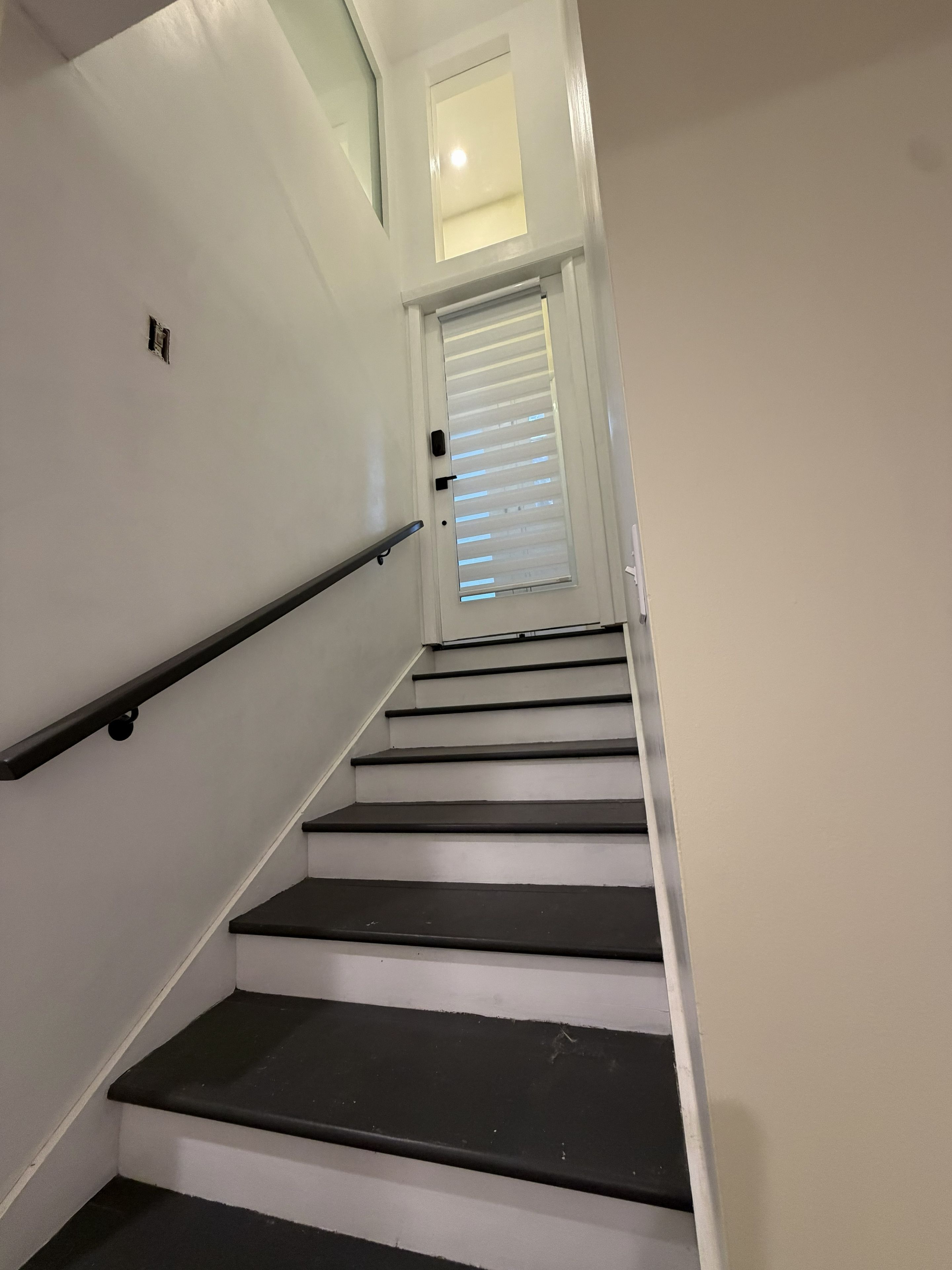 A staircase with a handrail, a door with blinds, and a small window at the top.
