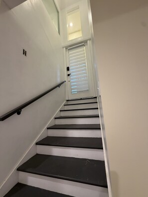 Una escalera con barandilla, una puerta con persianas y un pequeño ventanal en la parte superior.