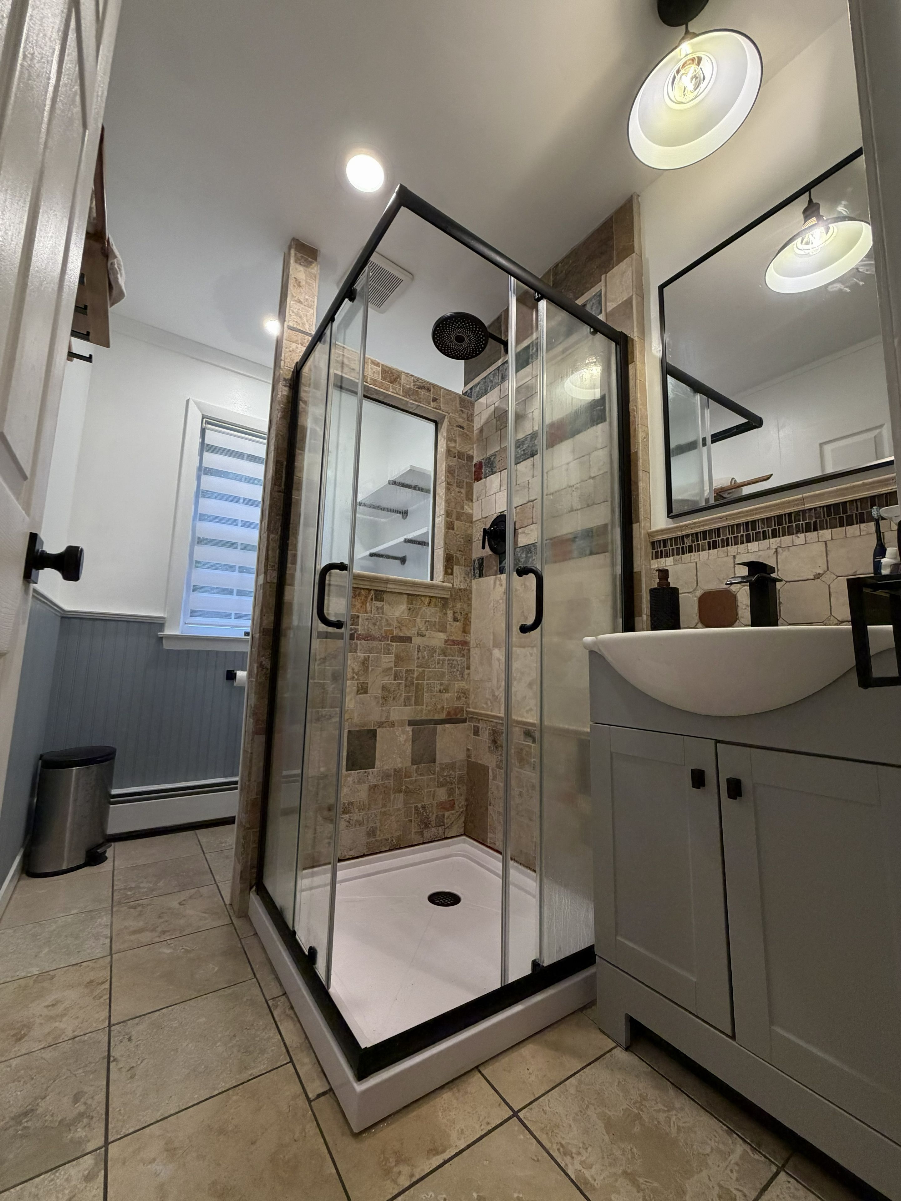 A modern bathroom with a glass-enclosed shower, a sink, and a mirror.