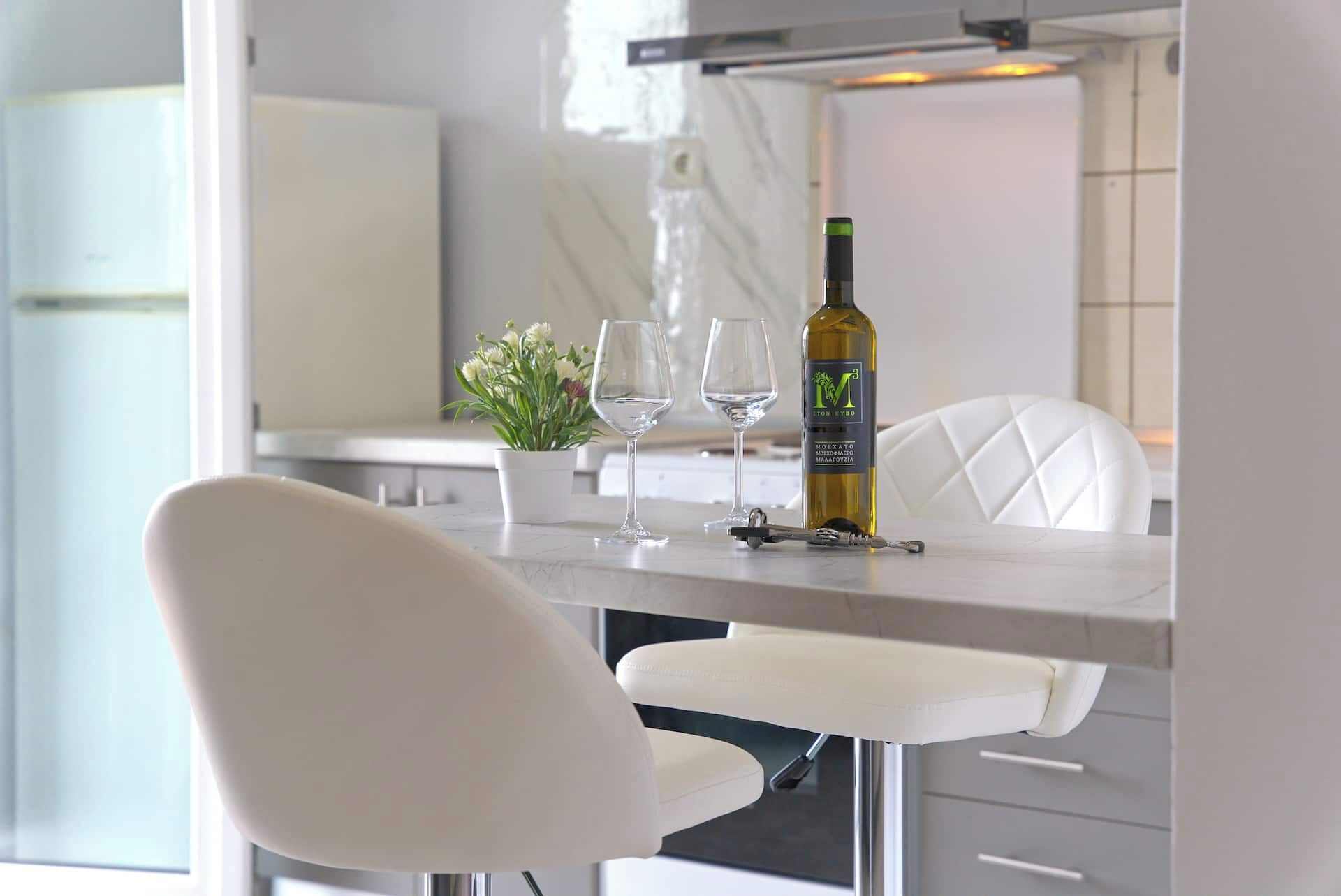 A modern kitchen with a dining table, two wine glasses, a bottle of wine, and a potted plant.