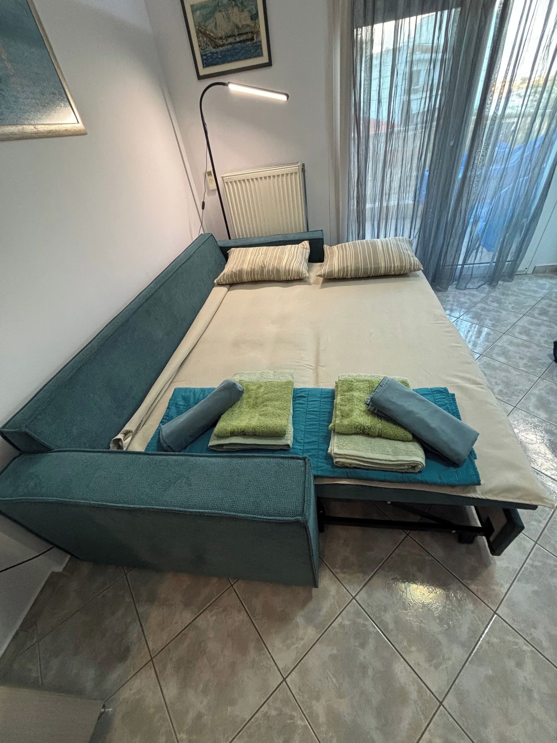Ein modernes Schlafzimmer mit Bett, Nachttisch, Heizkörper und einem Fenster mit Vorhängen.