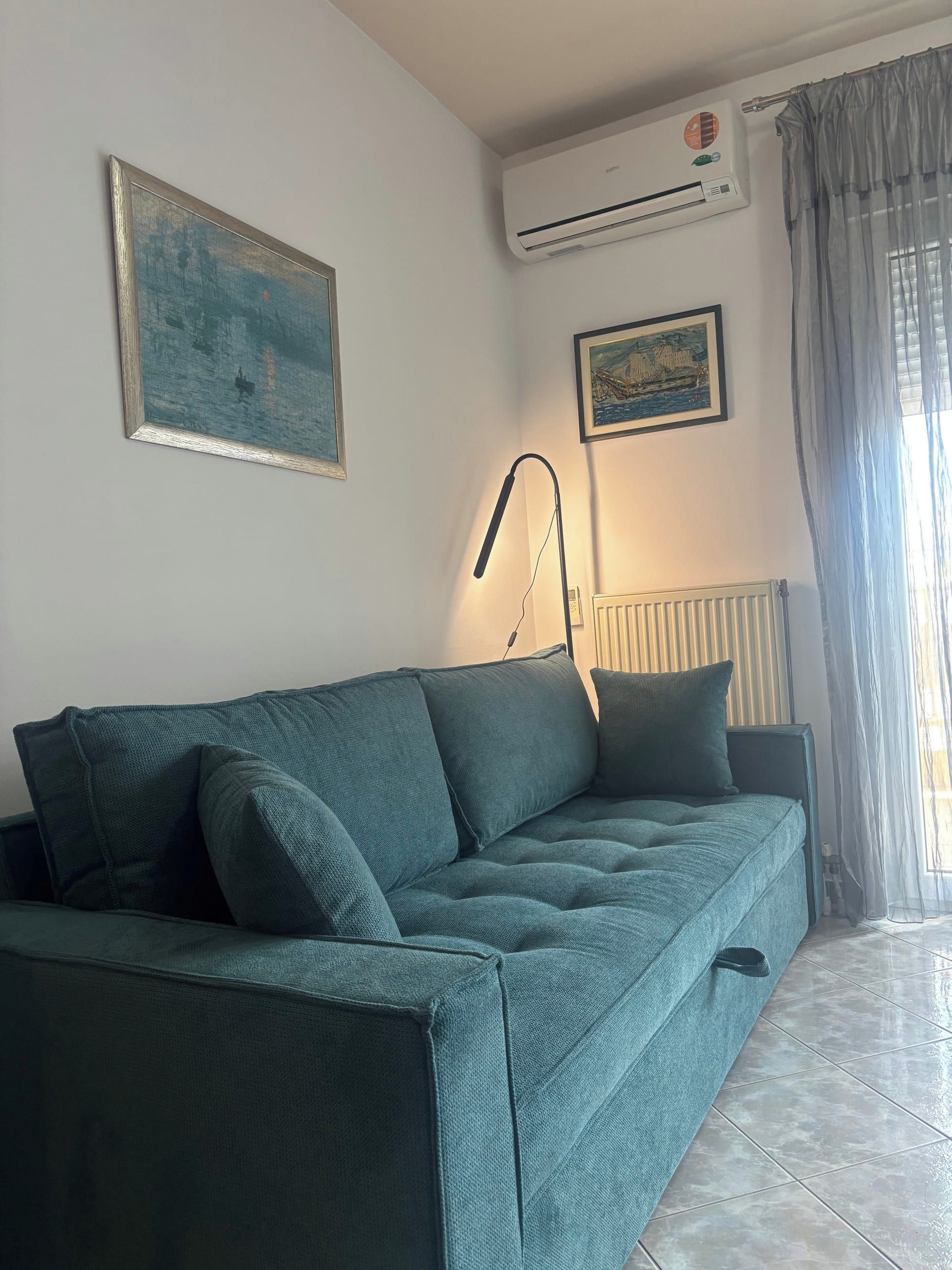 Ein Wohnzimmer mit einem grünen Sofa, einer stehenden Stehlampe und zwei Wandklimaanlagen.