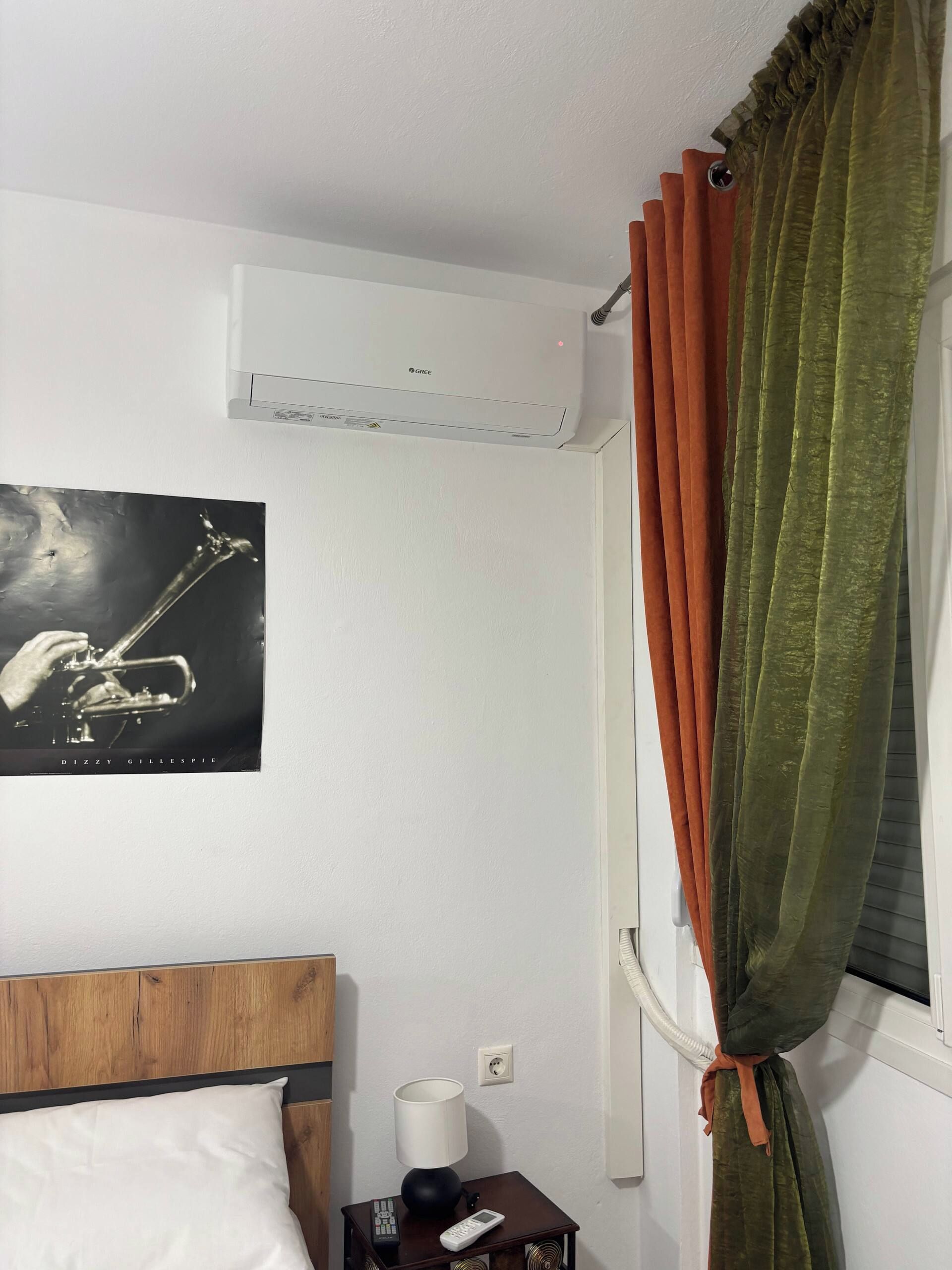 Ein Hotelzimmer mit einem Bett, einem Nachttisch mit Lampe, einer Fernbedienung, einer Wand-Klimaanlage und einem Fenster mit Vorhängen.