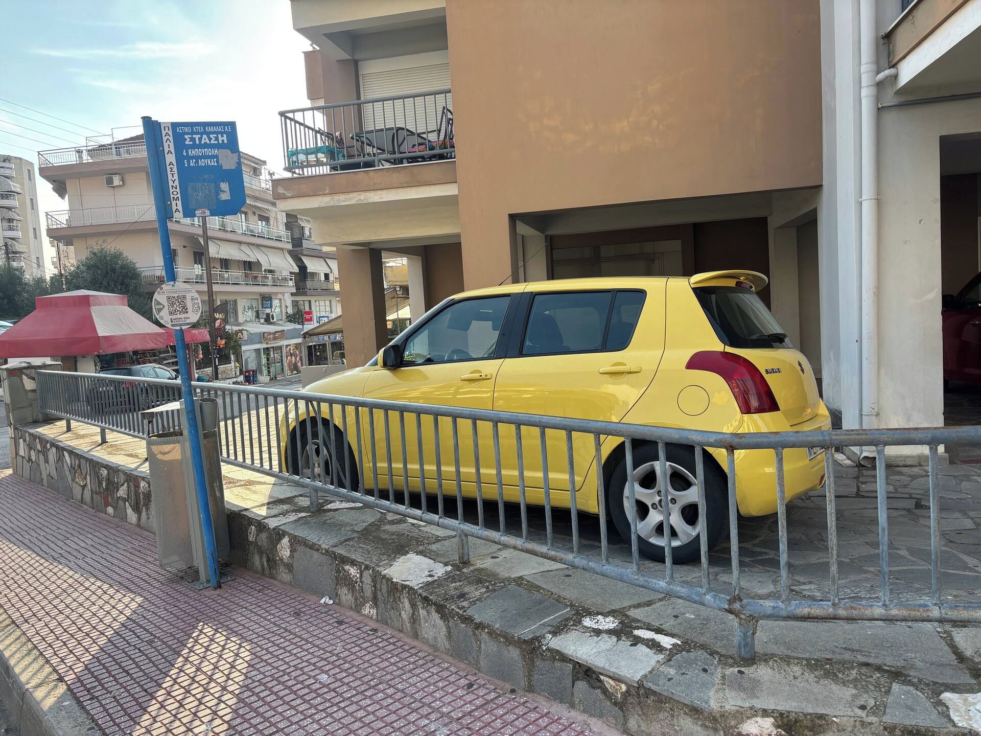 Un cotxe groc aparcat davant d'un edifici amb un rètol blau.