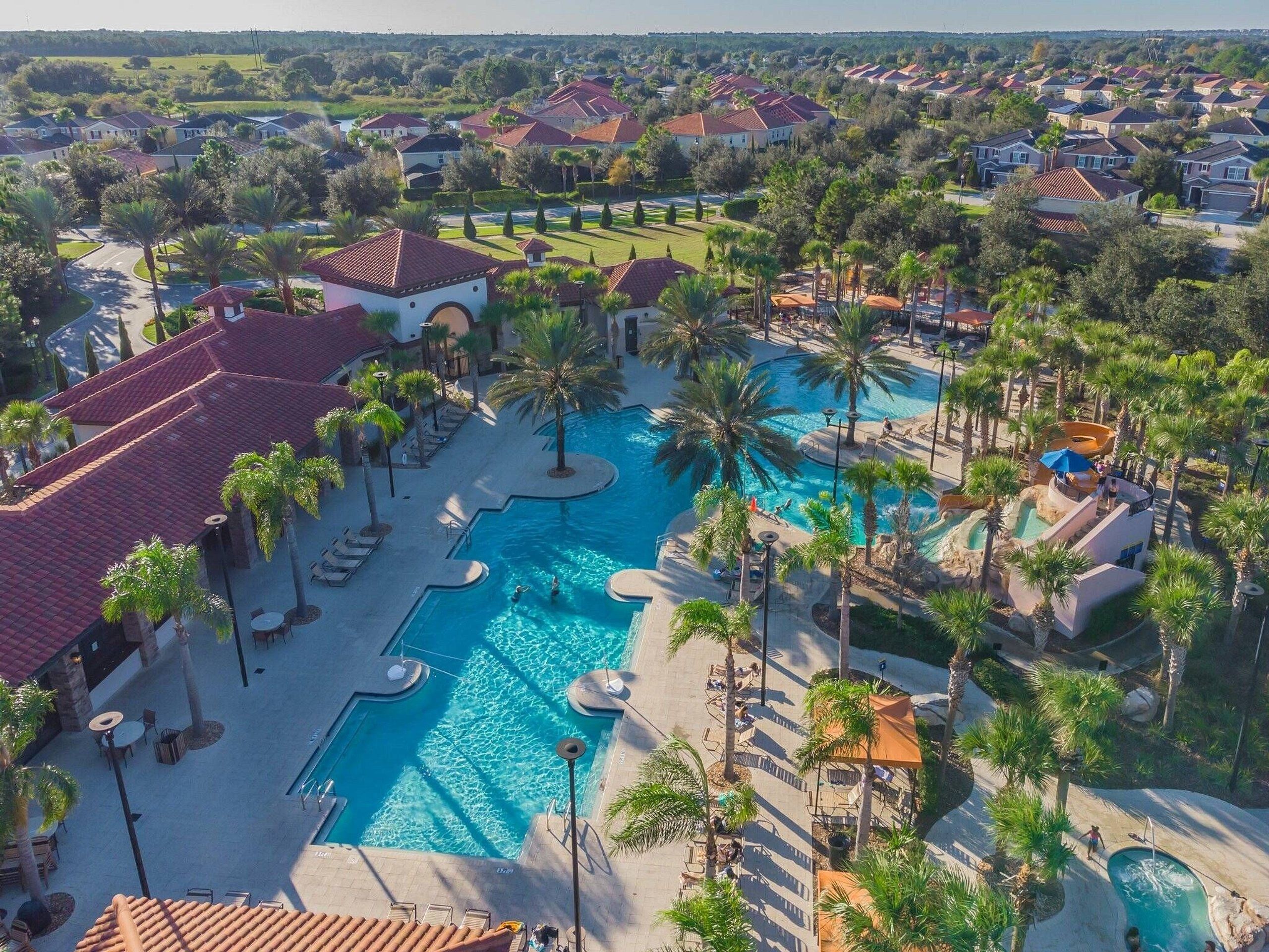 A resort with a large swimming pool, palm trees, and a view of surrounding houses.