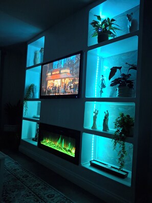Ein Wohnzimmer mit einem an der Wand befestigten Flachbildfernseher, umgeben von Regalen mit Pflanzen und Dekoration.