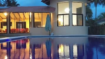 A building with a swimming pool in front, large windows, and a patio area with outdoor furniture.