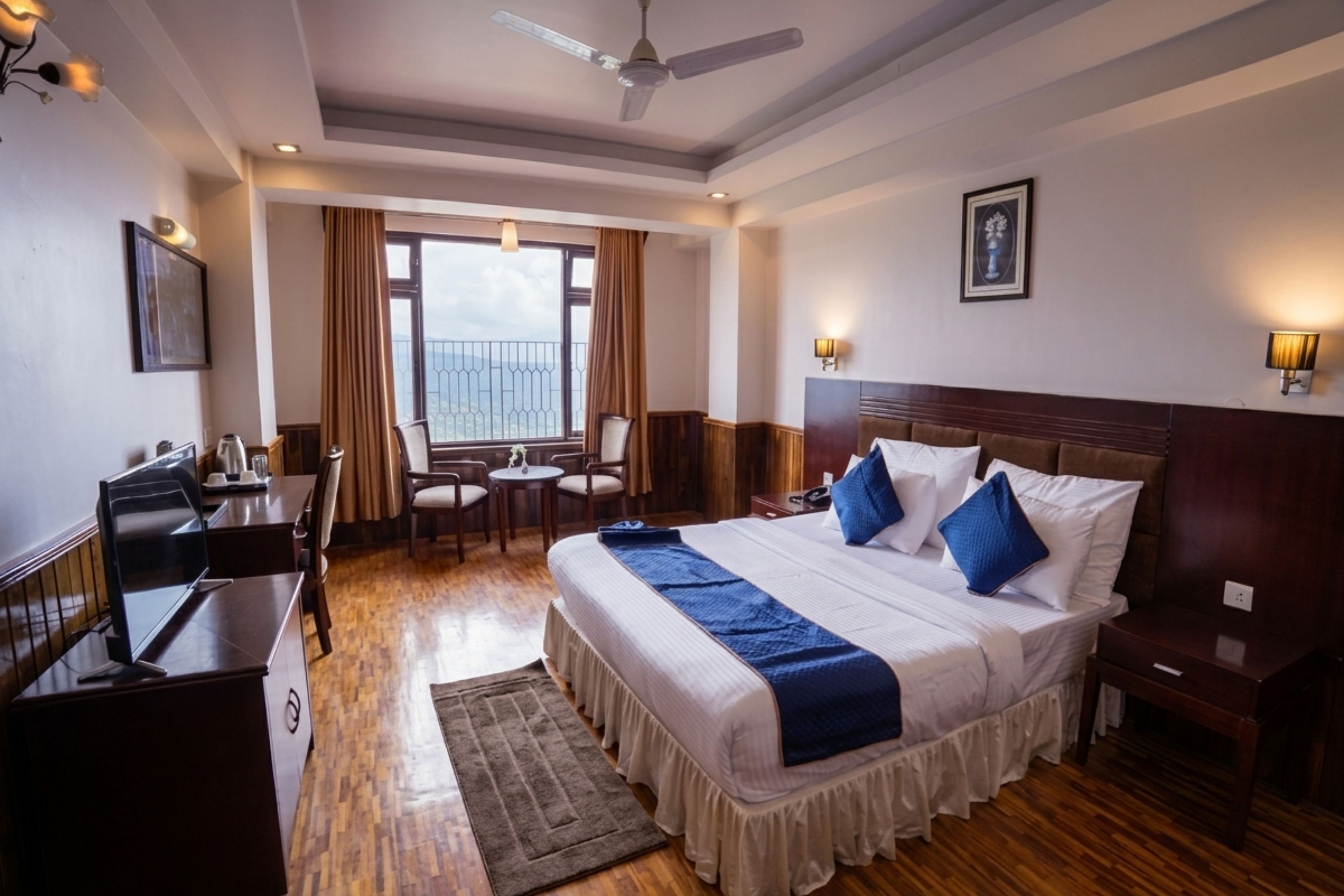 A hotel room with a bed, a desk, a chair, a small table, and a view of the outdoors.
