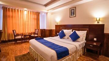 A hotel room with a large bed, a desk, a chair, and a window with curtains.