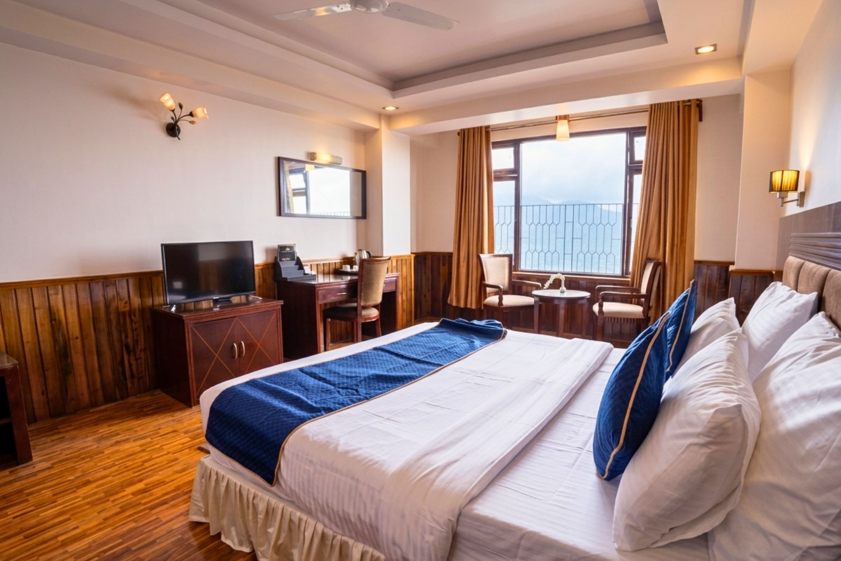 A hotel room with a large bed, a desk, a television, and a balcony with a view.