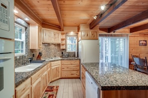 A kitchen with wooden cabinets, granite countertops, a refrigerator, and a window with a view of the outdoors. - Cozy 4-bedroom Cabin in Blue Lake Springs Arnold (Arnold)