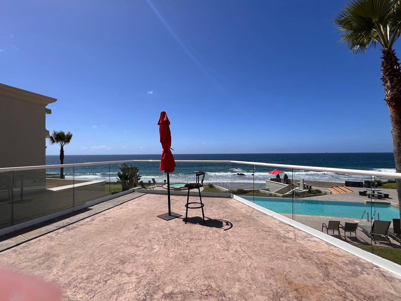Ein Balkon mit Glasgeländer, der einen Blick auf einen Pool und den Ozean bietet.