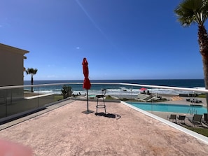 Ein Balkon mit Glasgeländer, der einen Blick auf einen Pool und den Ozean bietet.
