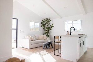 Een moderne woonruimte met een bank, een eethoek, een keuken met een spoelbak en een groot raam.