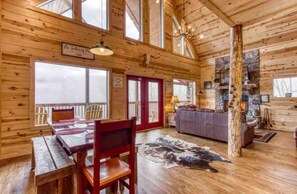 A log cabin interior with a dining area, a fireplace, and a large window. - Woodlands: 4 Person Special Offer (Gatlinburg)
