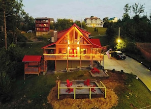 A two-story wooden cabin with a balcony, surrounded by a fenced yard with red chairs. - Woodlands: 4 Person Special Offer (Gatlinburg)