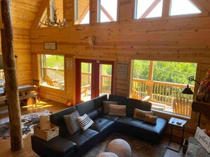 A cabin interior with a black leather sofa, wooden walls, and large windows. - Woodlands: 4 Person Special Offer (Gatlinburg)