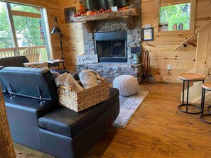 A cozy cabin interior with a fireplace, a leather sofa, a woven basket, and a stone wall. - Woodlands: 4 Person Special Offer (Gatlinburg)