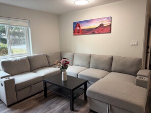 Een moderne woonkamer met een hoekbank, een bijzettafeltje en een schilderij van een woestijnlandschap.