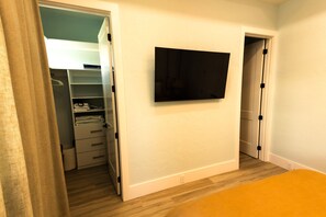 Un dormitorio con cama, televisor montado en la pared, armario con espacio para colgar y una puerta que da a otra habitación.