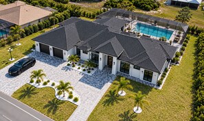 Ein modernes, zweistöckiges Haus mit Schwimmbad, Auffahrt und einem geparkten Auto davor.