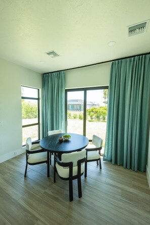 Una habitación con una mesa redonda, cuatro sillas, una ventana y vistas a una casa y follaje exterior.