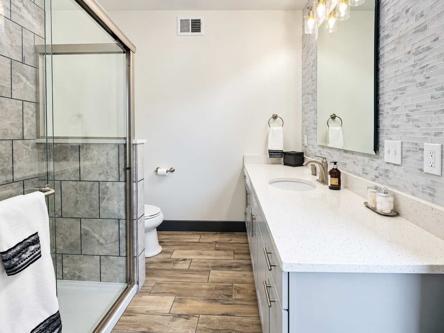 A modern bathroom with a glass shower enclosure, a white toilet, a double sink vanity, and a large mirror.