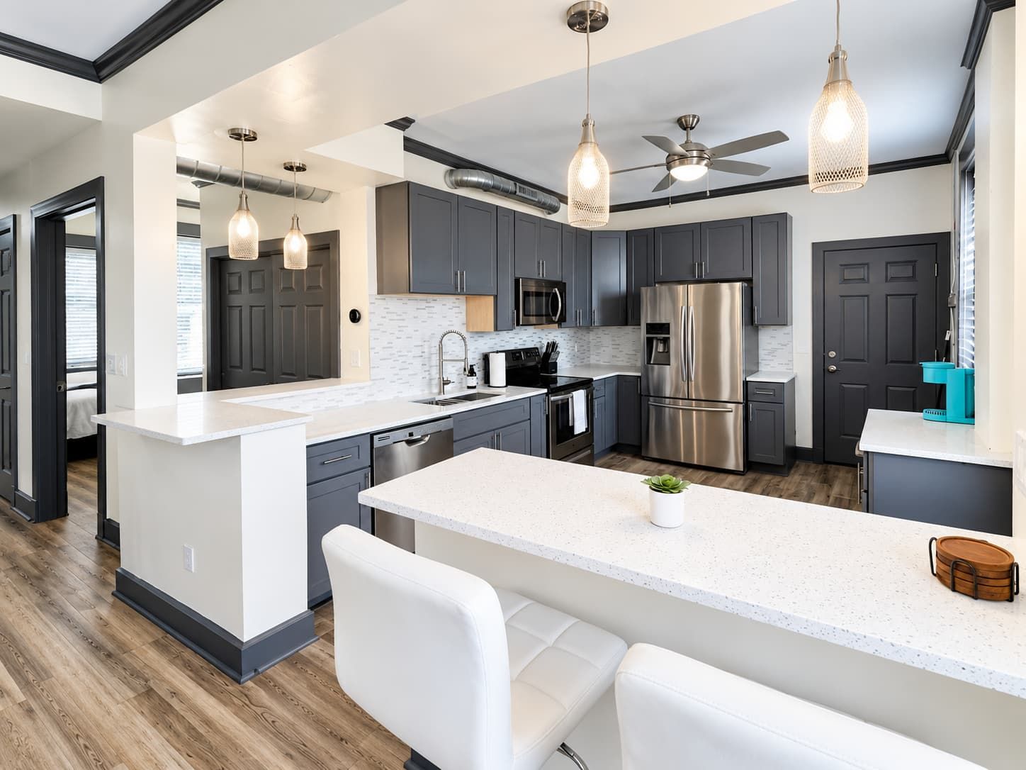 A modern kitchen with grey cabinets, stainless steel appliances, a white island, and pendant lighting.