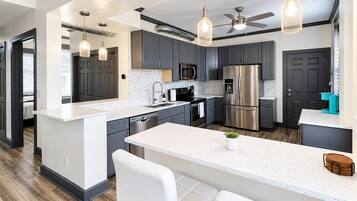A modern kitchen with grey cabinets, stainless steel appliances, a white island, and pendant lighting.