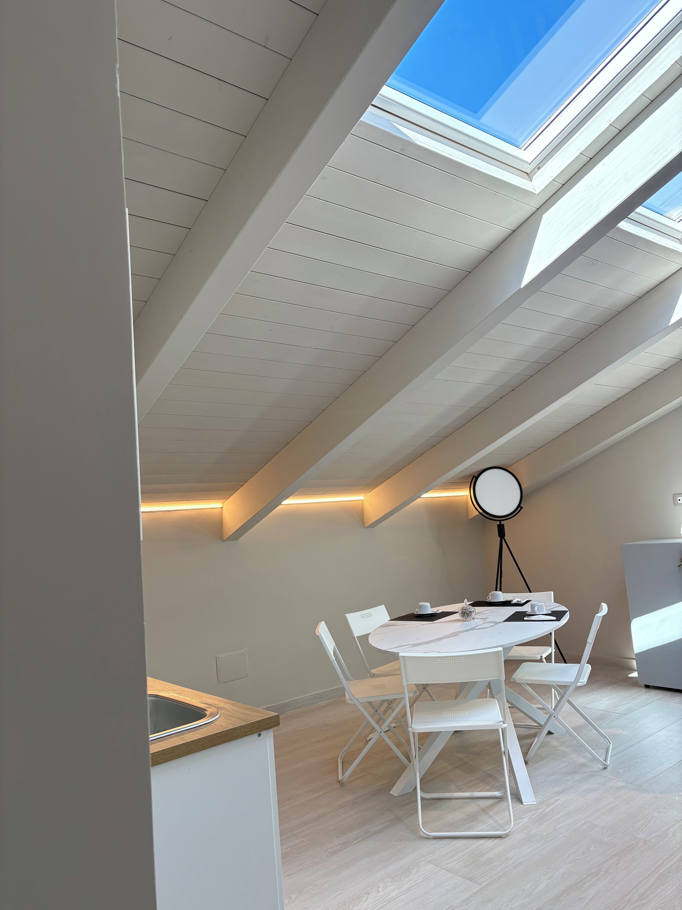 Ein Zimmer mit einem Oberlicht, einem runden Tisch mit Stühlen und einem Schreibtisch mit Waschbecken.