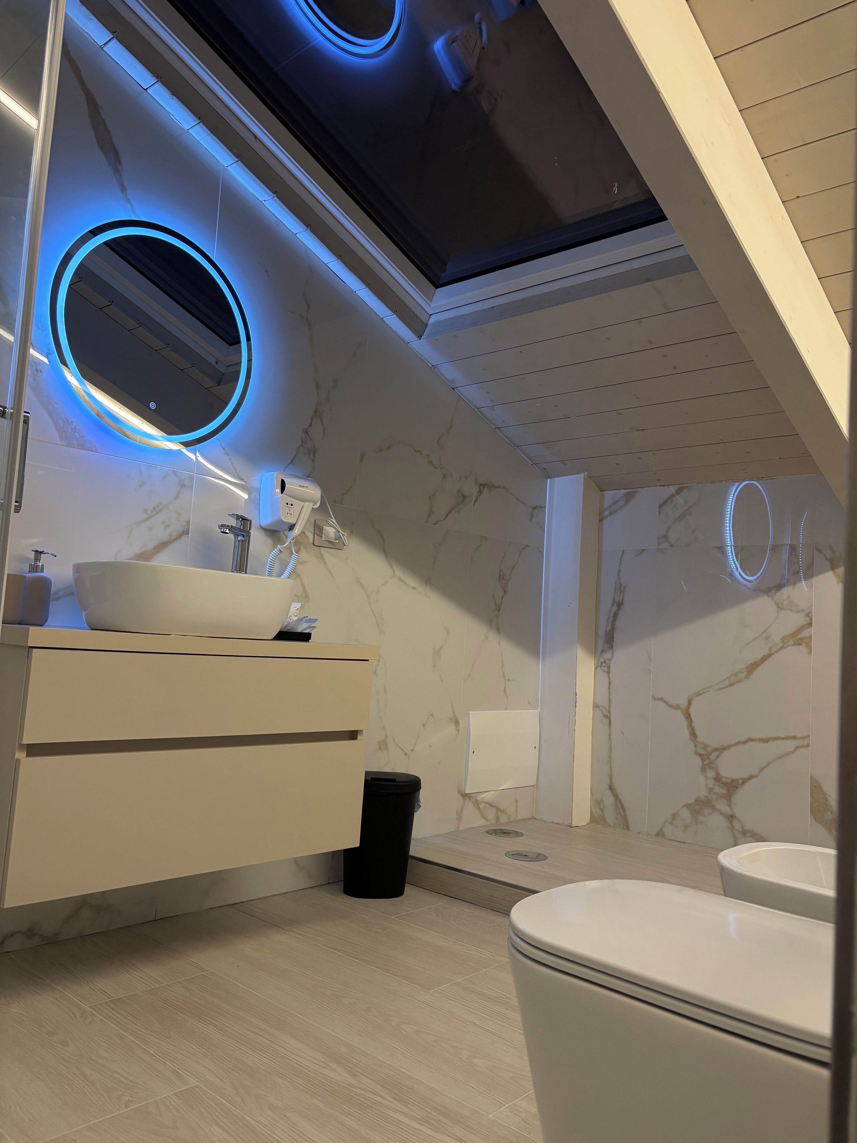 Un bagno moderno con un mobile vanitario bianco, uno specchio rotondo e un water.