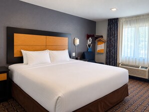Habitación de hotel con una cama grande, una mesita de noche, un escritorio, una silla, una ventana con cortinas y un calentador en la pared.