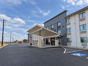 A modern hotel with a covered entrance, a parking lot, and a clear sky. - The Denton Inn (Denton)