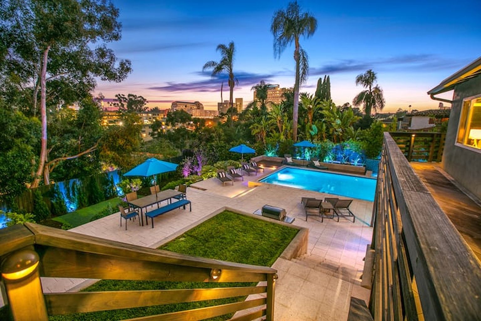 A pool area with lounge chairs and umbrellas, surrounded by greenery and palm trees.