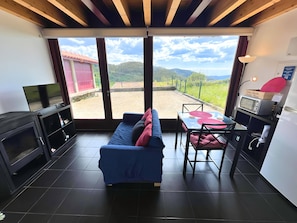 Habitació amb un sofà blau, televisió, taula amb cadires, microones i frigorífic.