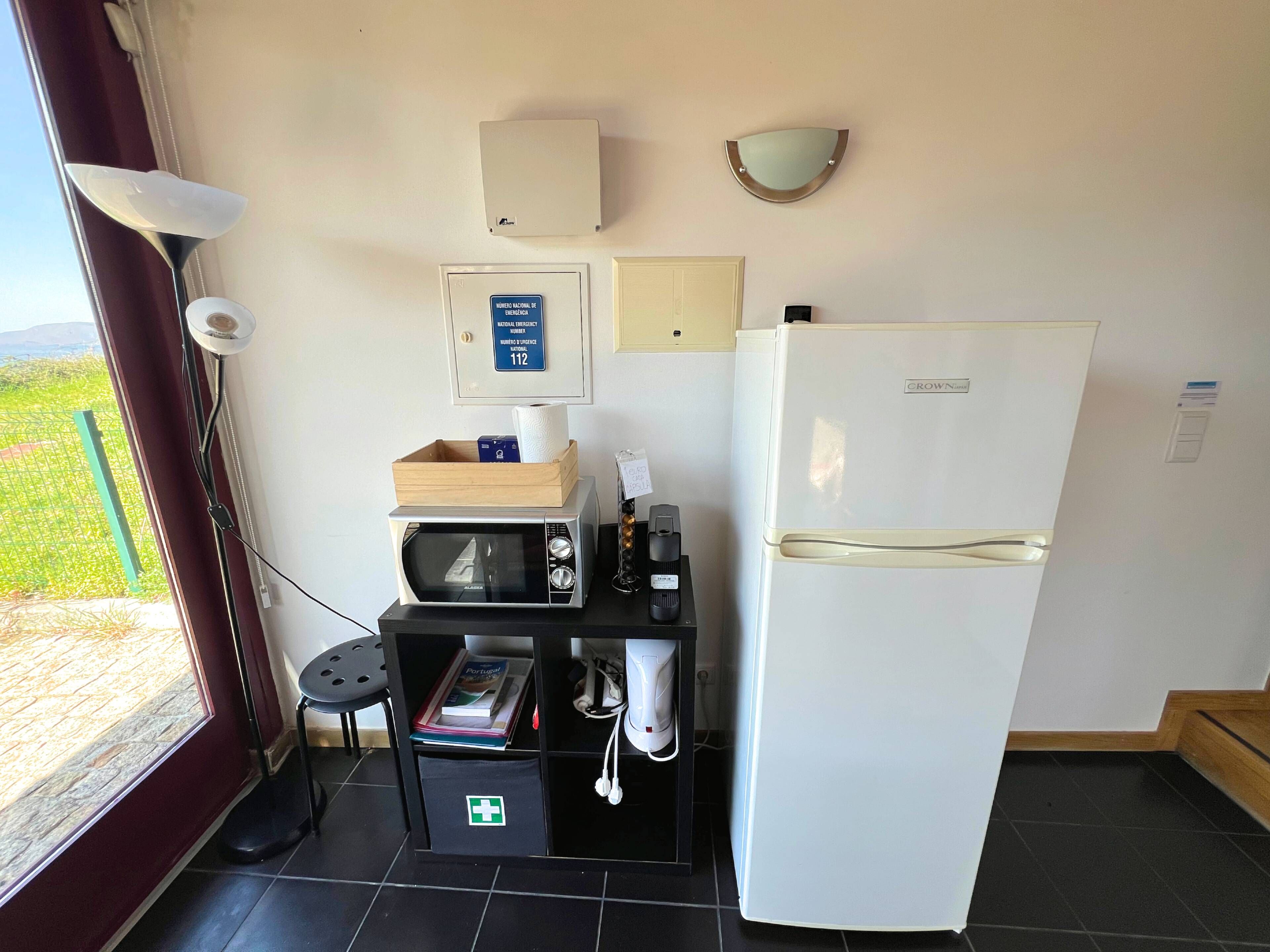 A kitchenette with a microwave, a refrigerator, a wooden box, and a first aid kit.