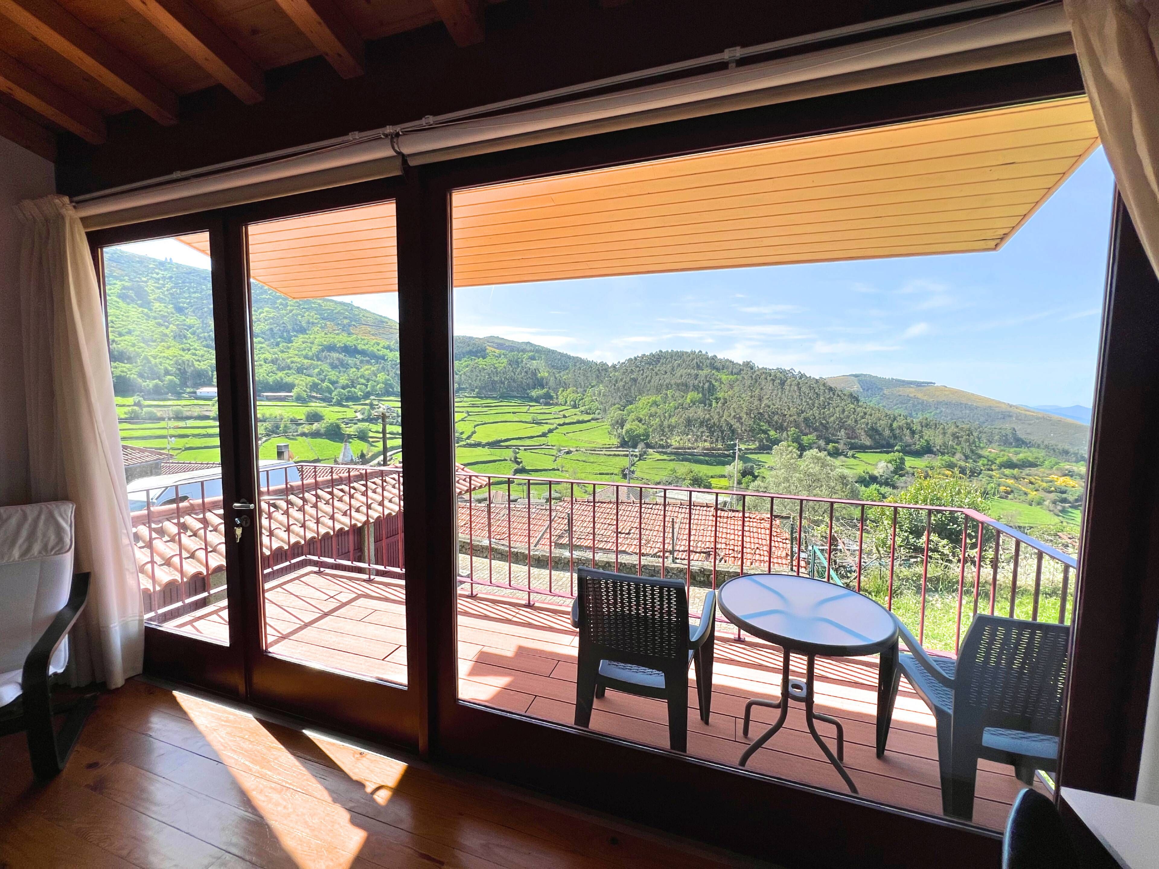 Una habitación con un gran ventanal corredero que da a una terraza exterior con mesa y sillas.