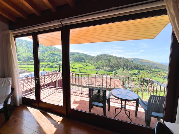 Una habitación con un gran ventanal corredero que da a una terraza exterior con mesa y sillas.