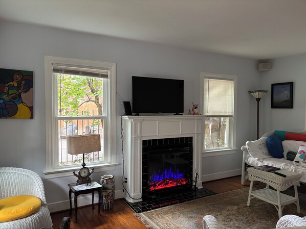 A living room with a fireplace, a television, and a window with a view of a tree. - Eclectic 2-bedroom house with delightful outside spaces in walkable Montrose (Houston)