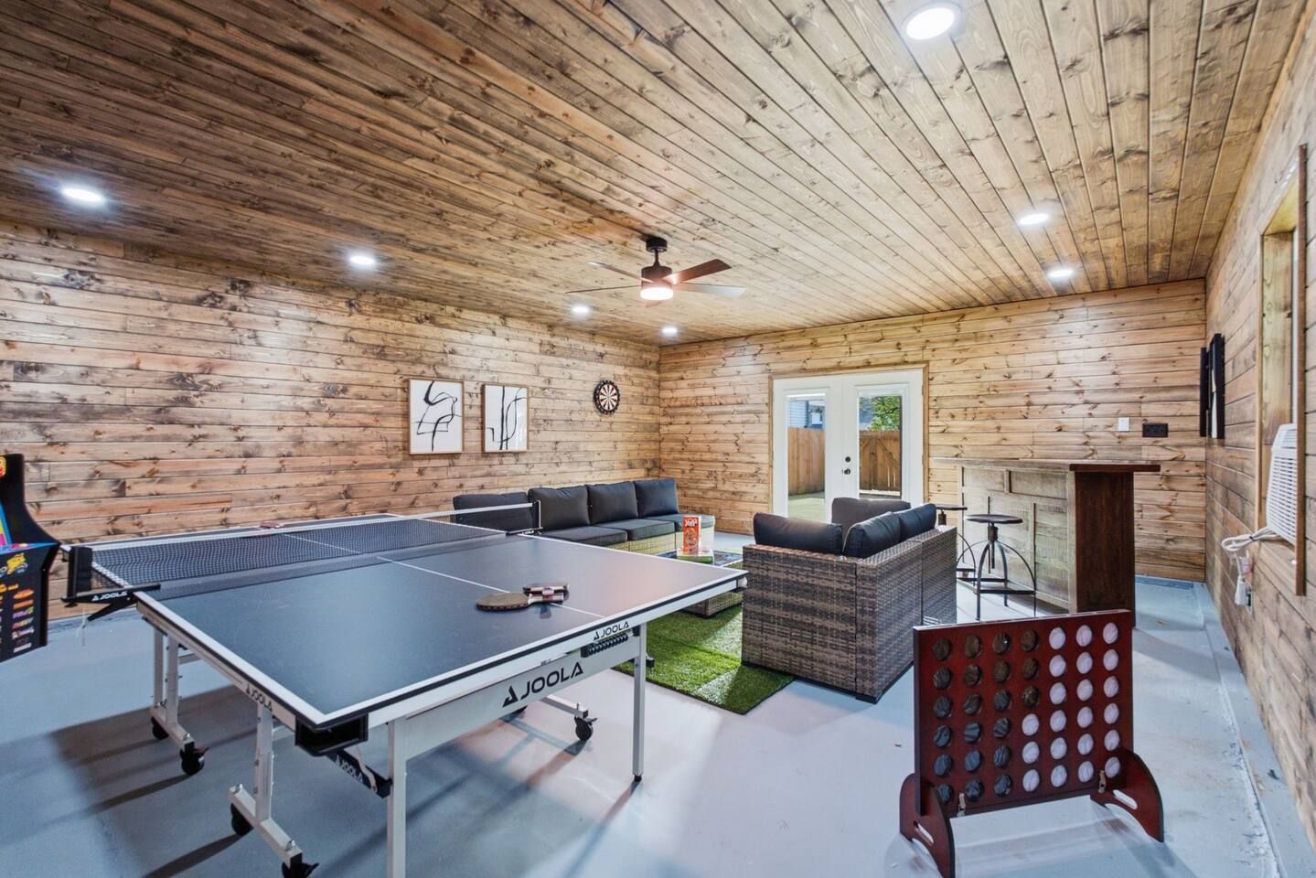 A ping pong table in a room with wooden walls, a ceiling fan, and a door leading outside.