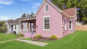 A two-story house with a pink exterior, a front porch, and a well-maintained lawn.