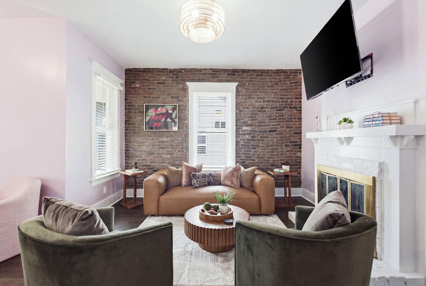A living room with a brick wall, a fireplace, a television mounted on the wall, and a sofa with multiple cushions.
