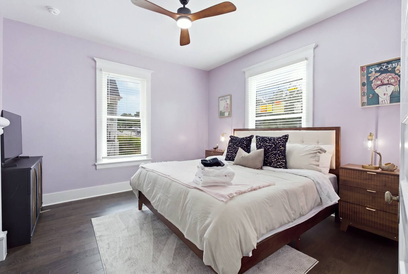A bedroom with a bed, bedside tables, a ceiling fan, and windows with blinds.