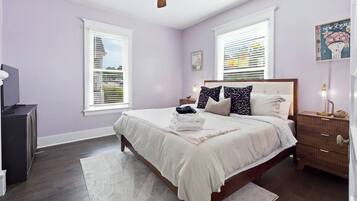 A bedroom with a bed, bedside tables, a ceiling fan, and windows with blinds.