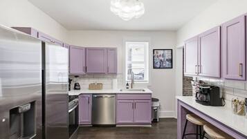 A modern kitchen with purple cabinets, stainless steel appliances, and a bar area with stools.