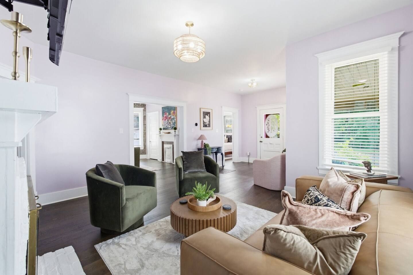Een ruime woonkamer met een open haard, een ronde salontafel en een groot raam met zonwering.