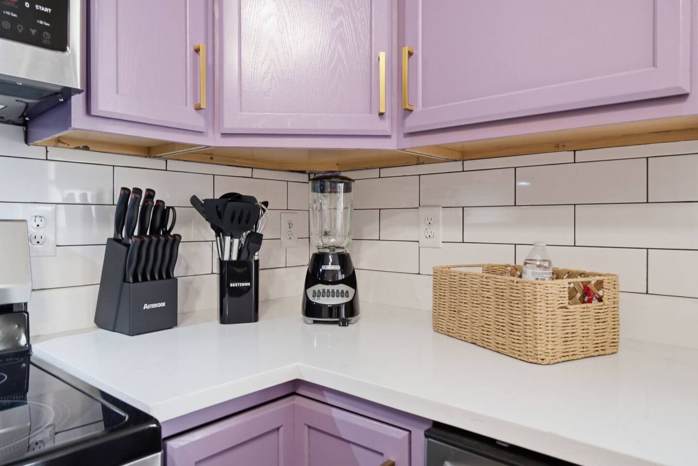 Een keuken met witte tegels, een blender, een messenblok en een rieten mand.