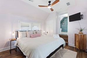 A bedroom with a bed, bedside tables, a ceiling fan, a TV mounted on the wall, and a view of the outside. - Hot Tub + 2 Kings | Near KY Horse Park | 3BR (Georgetown)