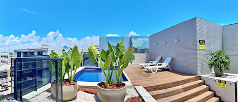 A rooftop pool area with lounge chairs, potted plants, and a view of the cityscape.